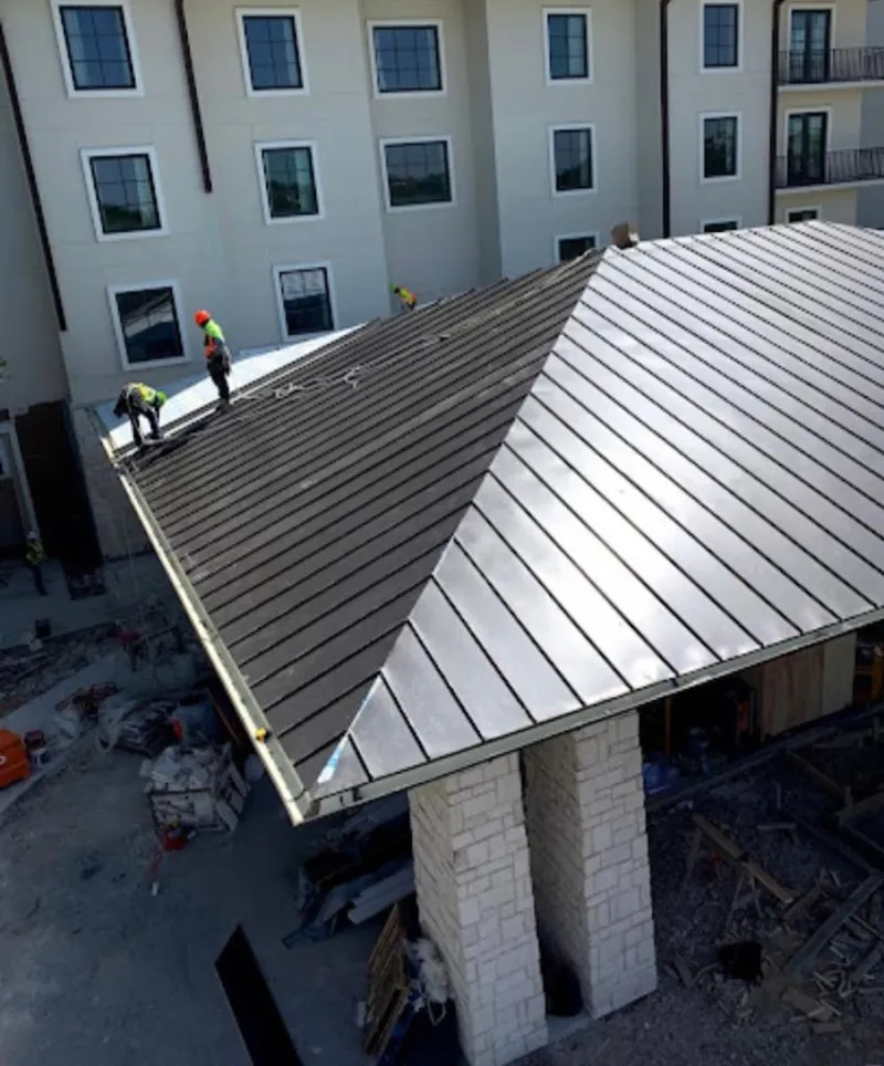 Crew installing standing seam metal roof panels on a commercial project in Anna